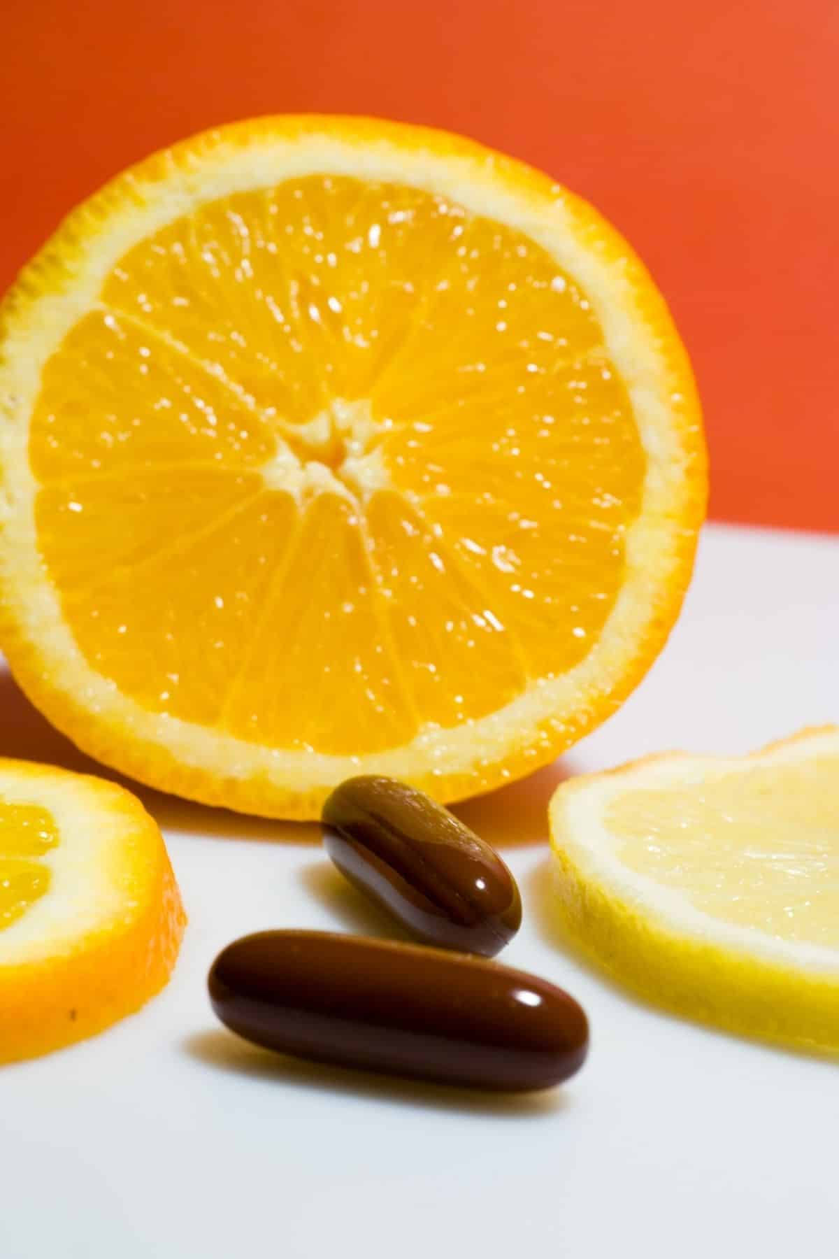 cápsulas de vitamina c frente a una naranja en rodajas.