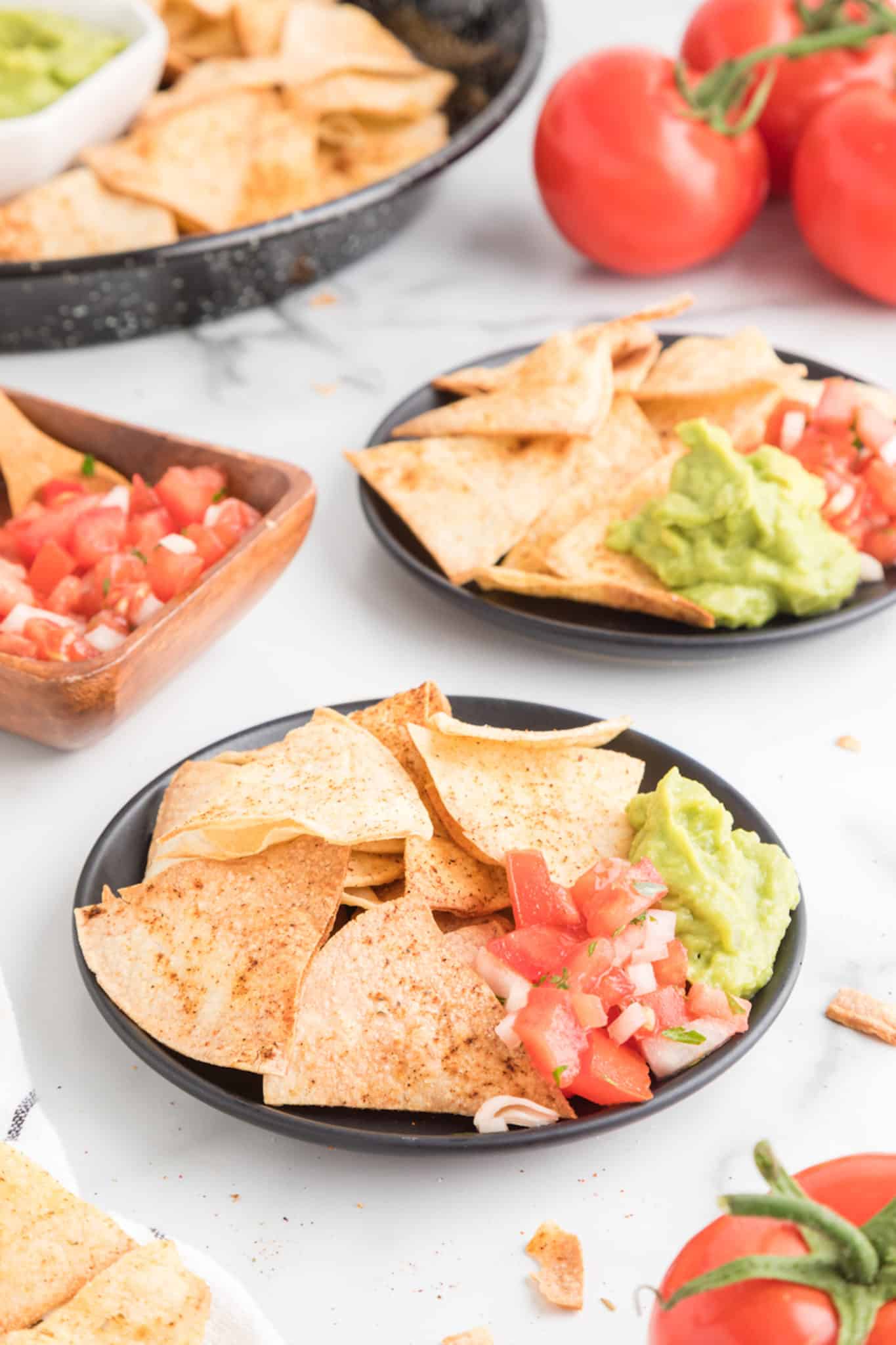 Dos pequeños platos negros de totopos frescos con salsa y guacamole.