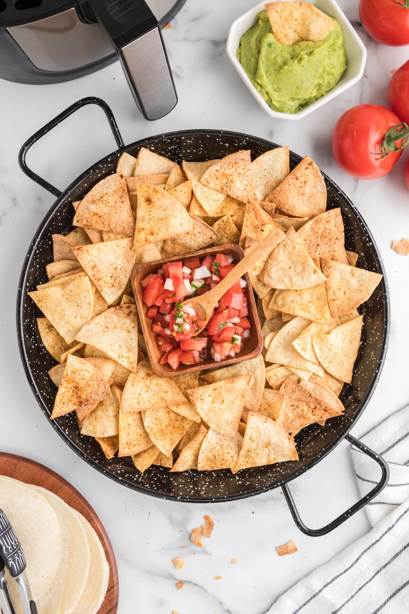 Vista superior de una gran fuente negra de chips de tortilla frescos que rodean un tazón de salsa.