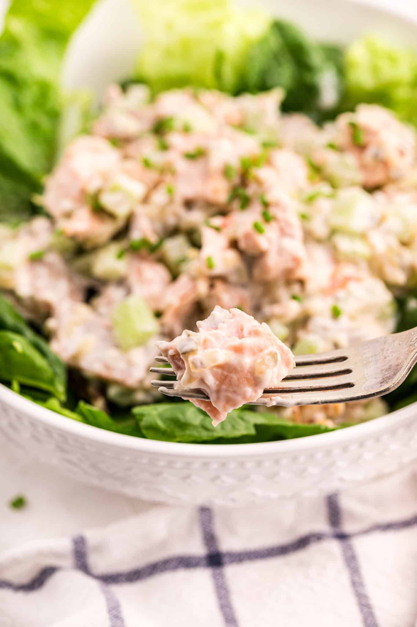 Un tenedor con un bocado de ensalada de salmón sobre un bol lleno.