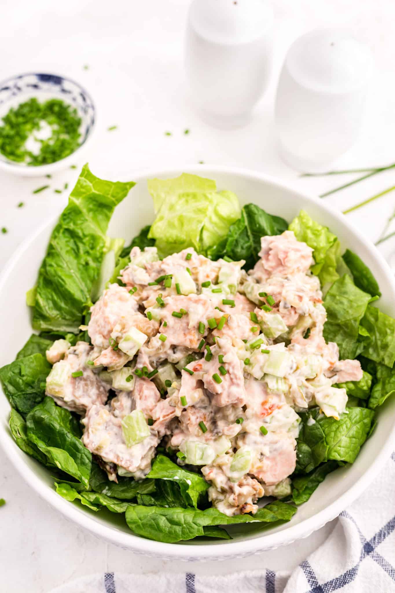 Una gran ensaladera blanca llena de verduras cubierta con ensalada de salmón.