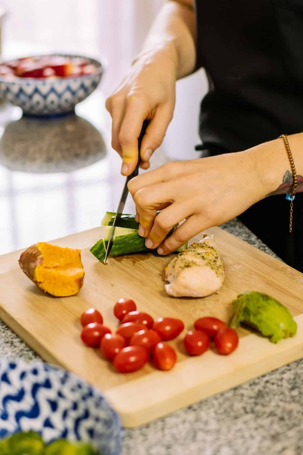 mujer preparando verduras en una tabla de cortar de madera.