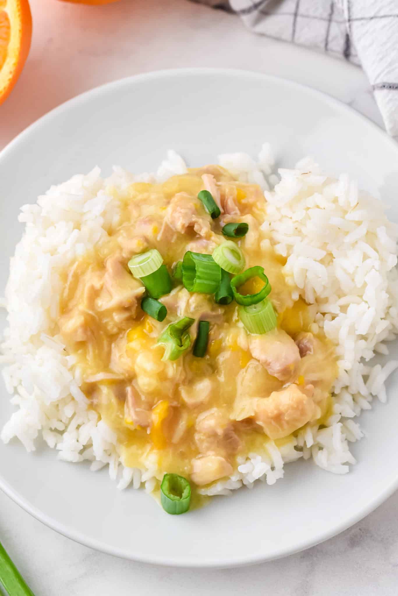 porción de pollo a la naranja sobre arroz blanco con cebollas verdes.