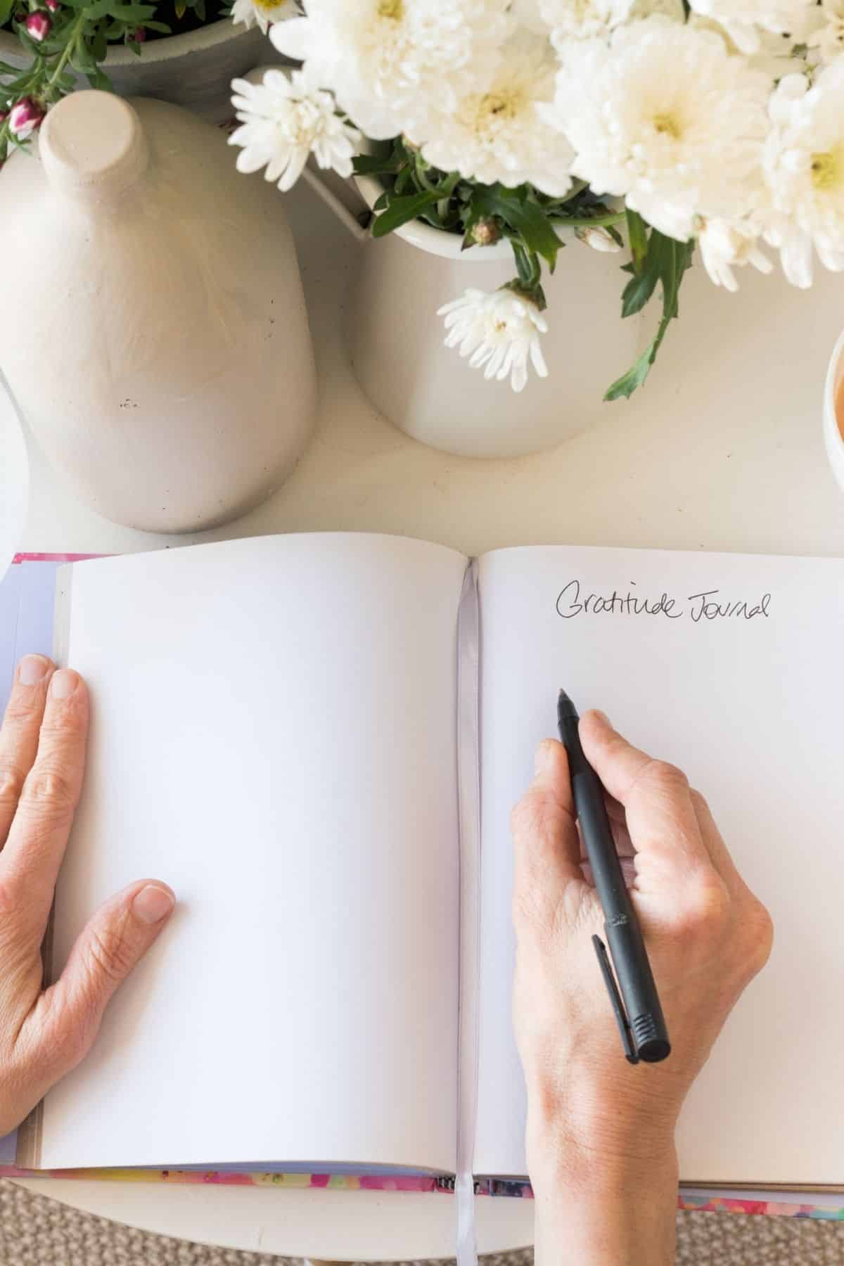 mujer escribiendo en un diario sobre una mesa blanca con flores.