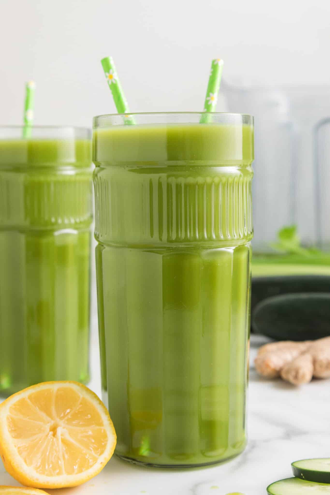 Dos vasos altos de jugo de limón, jengibre y verde, cada uno con dos pajitas.